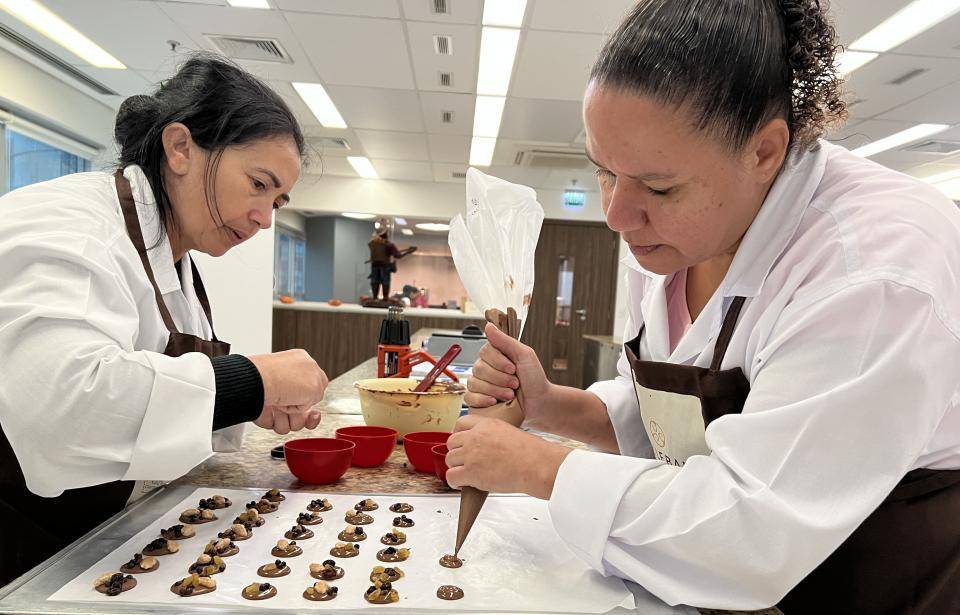 duas pessoas trabalhando com chocolate em cima da bancada