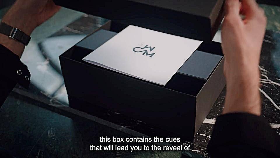 A chef's hands removing the lid of a box. A square card with the WCM logo on the front is inside