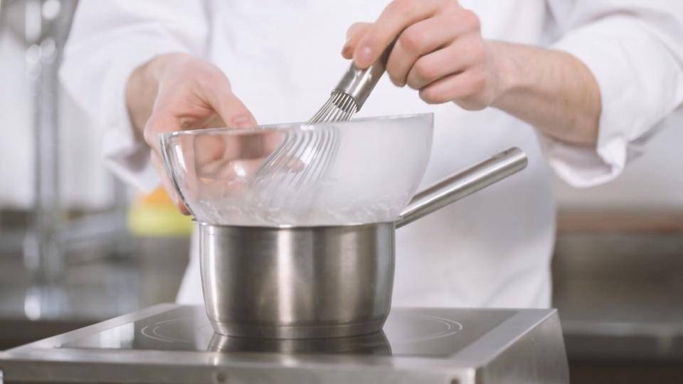 A chef whisks egg whites over a water bath