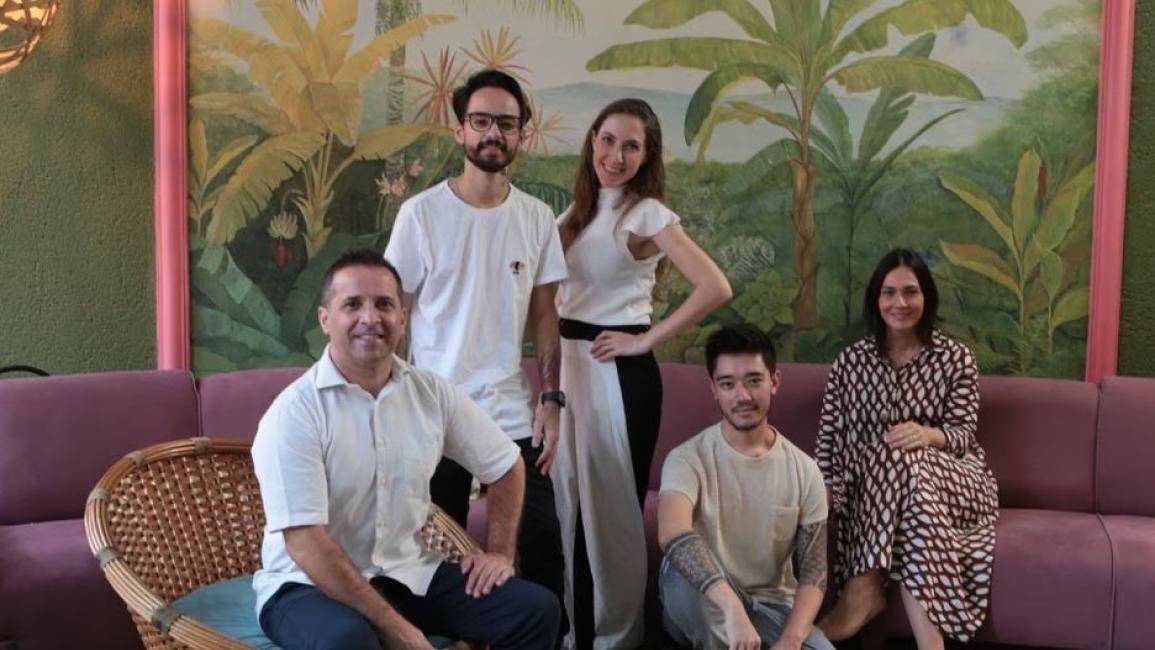 Três chefs sentados e dois de pé em frente a um quadro de bananeiras verdes