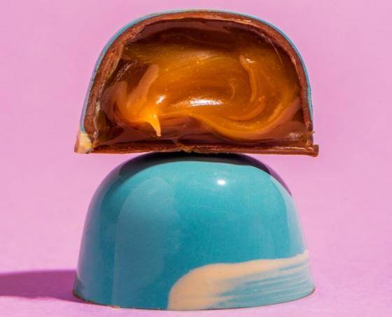 bombom cortado ao meio, embaixo a casquinha inteira vermelha com pincelada branca e a parte de cima apenas metade postrando recheio cremoso
